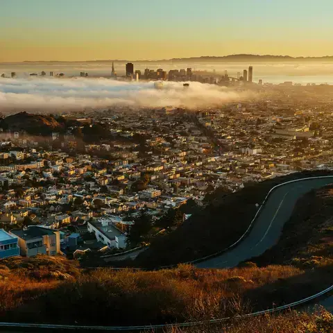 Cityscape at sunrise with fog covering the downtown area, viewed from a winding hilltop road