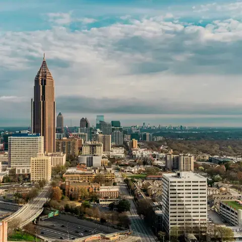 Atlanta skyline on a cloudy day, featuring tall buildings and sprawling residential areas, with lush greenery in the distance