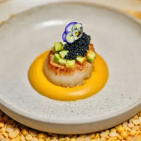 Gourmet scallop dish with edible flower and caviar garnish.