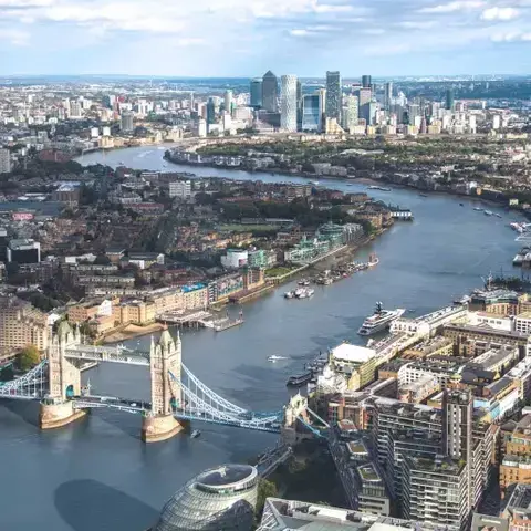 Aerial view of London featuring the iconic Tower Bridge, Thames River, and modern cityscape of Canary Wharf in the background