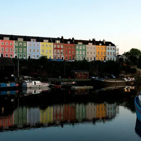 Colorful houses in Bristol reflect on the calm waters of the harbor, creating a vibrant and picturesque evening scene